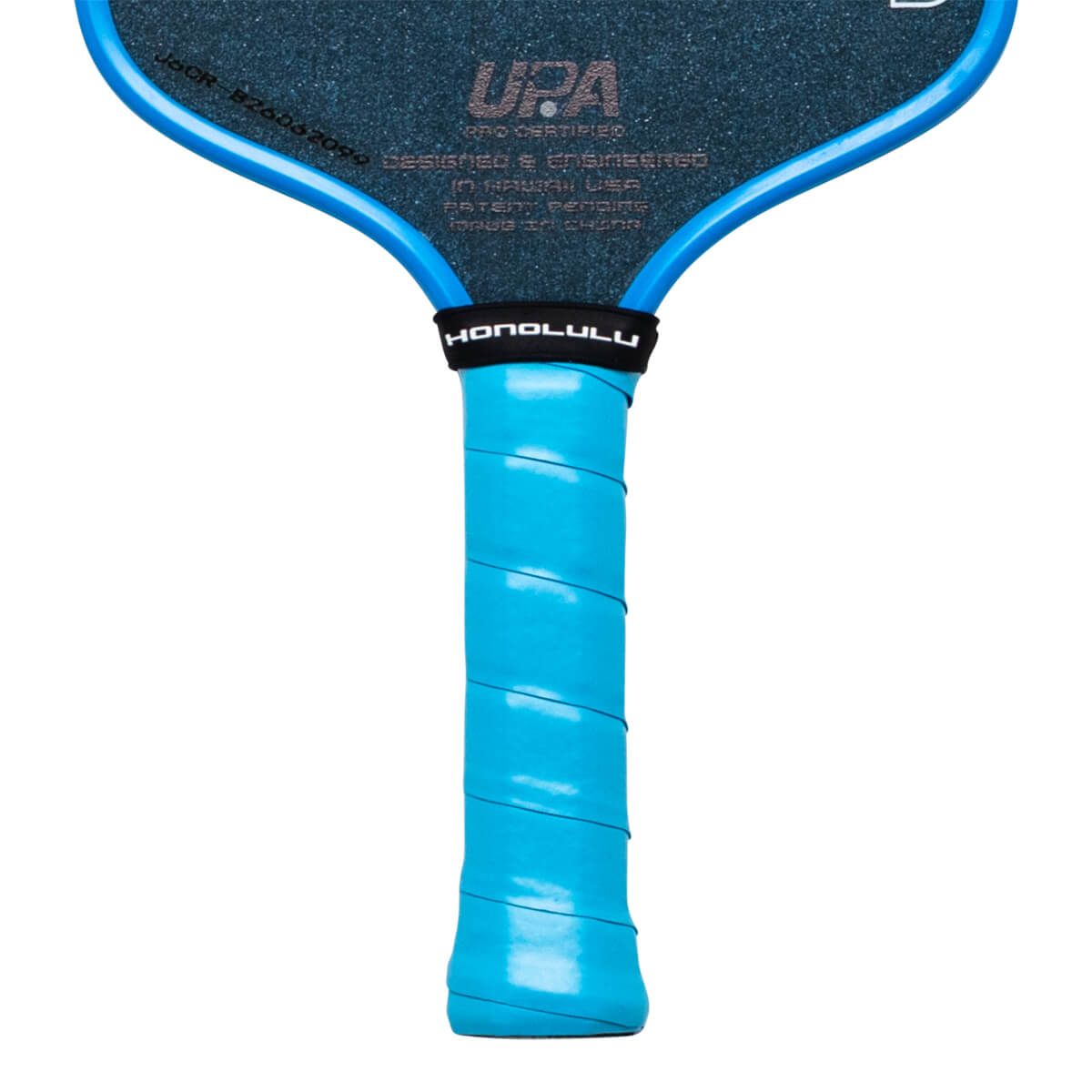 Close-up of a pickleball paddle showing the blue grip, "HONOLULU" text on a black band, and "UPA" logo.
