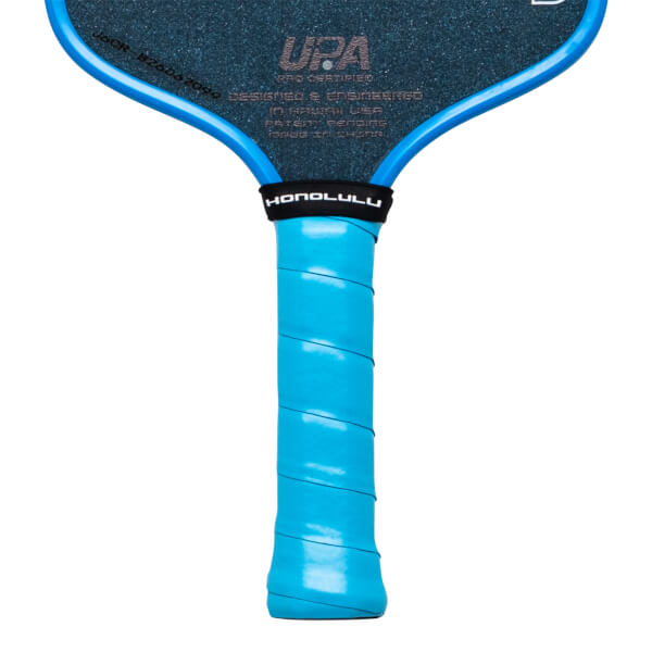 Close-up of a pickleball paddle showing the blue grip, "HONOLULU" text on a black band, and "UPA" logo.