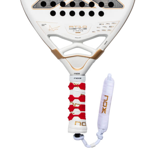 Close-up of the lower white racket face and handle featuring gold "AT10 GENIUS" branding, a red patterned grip, and a white wrist strap with gold "NOX" lettering.