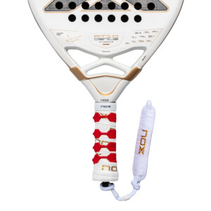 Close-up of the lower white racket face and handle featuring gold "AT10 GENIUS" branding, a red patterned grip, and a white wrist strap with gold "NOX" lettering.