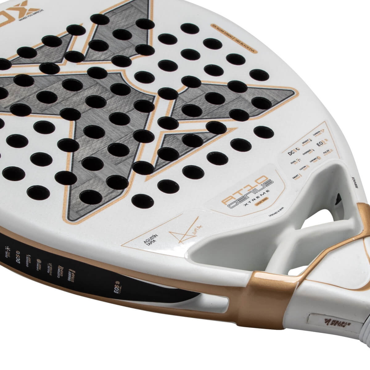 Close-up angled view of the white padel racket face featuring a large gray and gold X logo, black holes, and AT10 GENIUS XTREME text near its gold-accented throat.