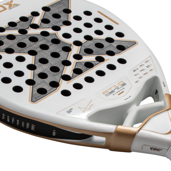 Close-up angled view of the white padel racket face featuring a large gray and gold X logo, black holes, and AT10 GENIUS XTREME text near its gold-accented throat.