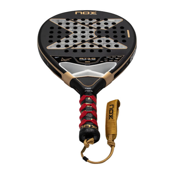 Front view of the black and gold Nox AT10 Genius padel racket featuring a large silver X logo, a red-patterned grip, and a gold wrist strap with the NOX brand name.