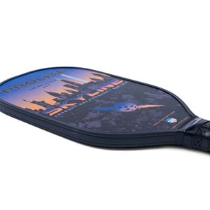 Corner view of a dark blue pickleball paddle with a skyline graphic, PROLITE text, and USAPA APPROVED label.