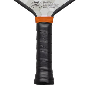 Close-up of pickleball paddle handle with black grip, orange band, and "USA PICKLEBALL APPROVED" text.