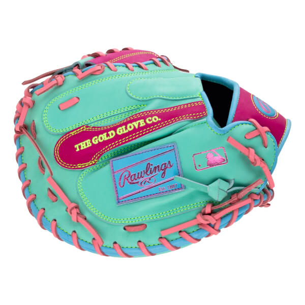 Back view of a mint green catcher's mitt with pink and blue accents, featuring the text "THE GOLD GLOVE CO." and a blue Rawlings logo patch.