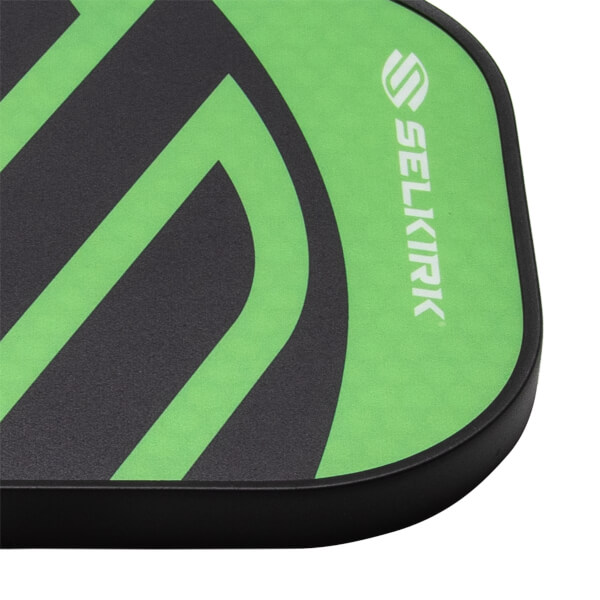 Close-up of a green and black pickleball paddle face with SELKIRK branding, a bold geometric pattern, and a black edge guard.