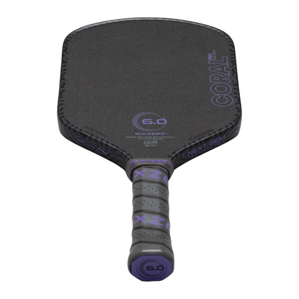 Top-down view of a black pickleball paddle with purple "CORAL PRO" text and a "6.0" logo.