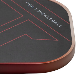 Close-up of a pickleball paddle corner showing red geometric lines and "TIER 1 PICKLEBALL" text on a dark surface.