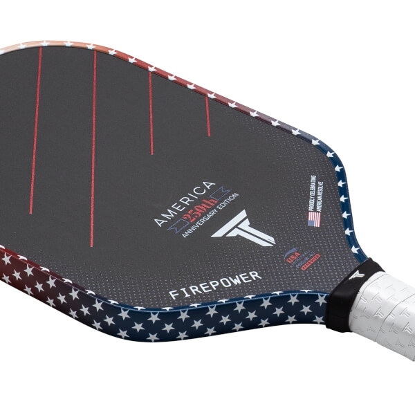 Corner view of a pickleball paddle featuring a dark surface with red stripes, "AMERICA 250th ANNIVERSARY EDITION," and a white star pattern along the edge.