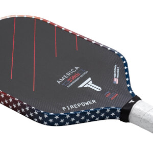 Corner view of a pickleball paddle featuring a dark surface with red stripes, "AMERICA 250th ANNIVERSARY EDITION," and a white star pattern along the edge.