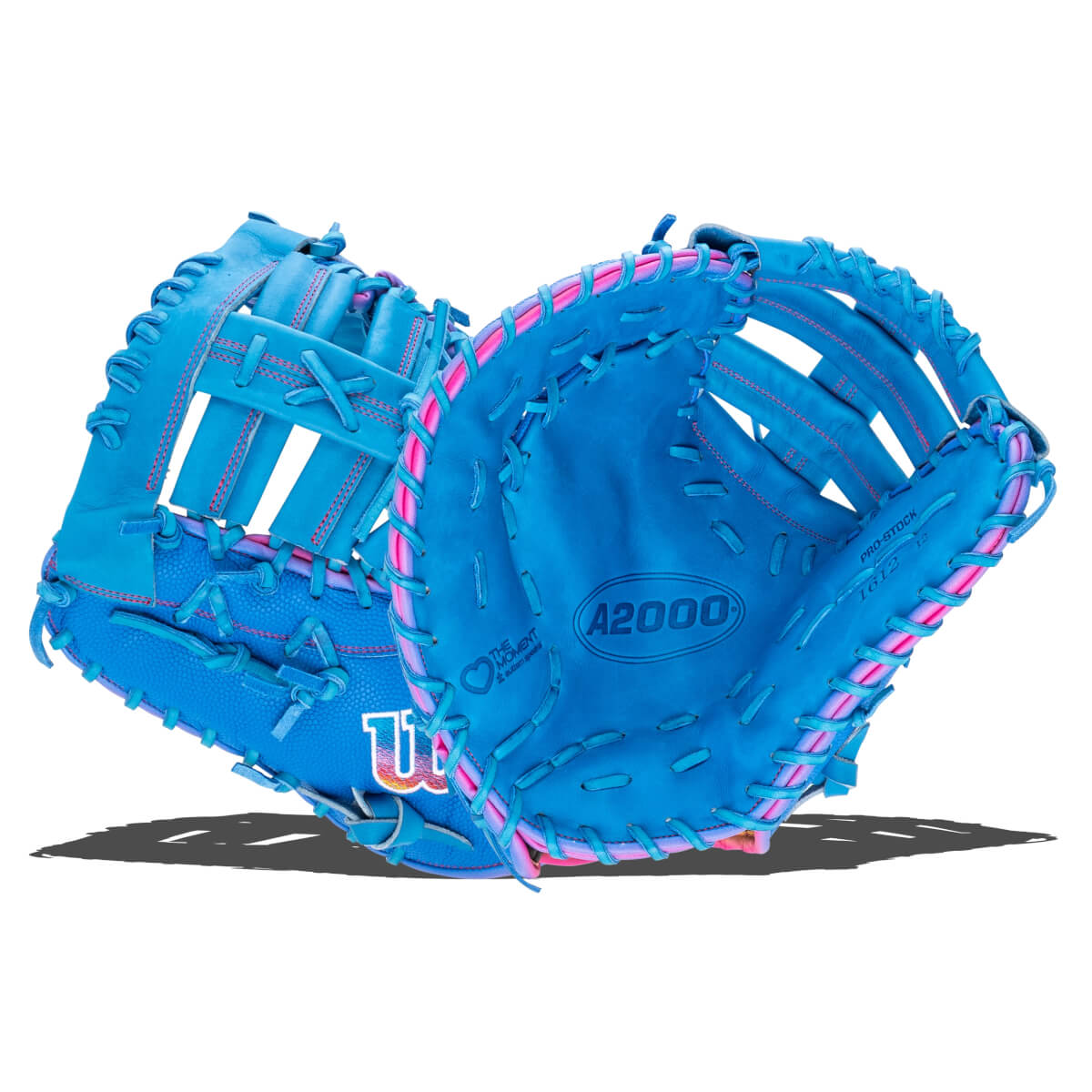 Front and side view of a blue A2000 first base mitt with pink accents, featuring the Wilson "W" logo and "THE MOMENT autism speaks" text on the palm.
