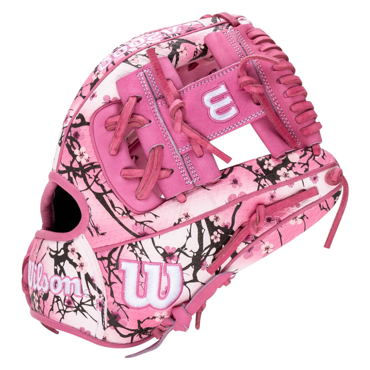 Back-side view of a pink baseball glove featuring a black cherry blossom branch pattern and white Wilson and 'W' logos.