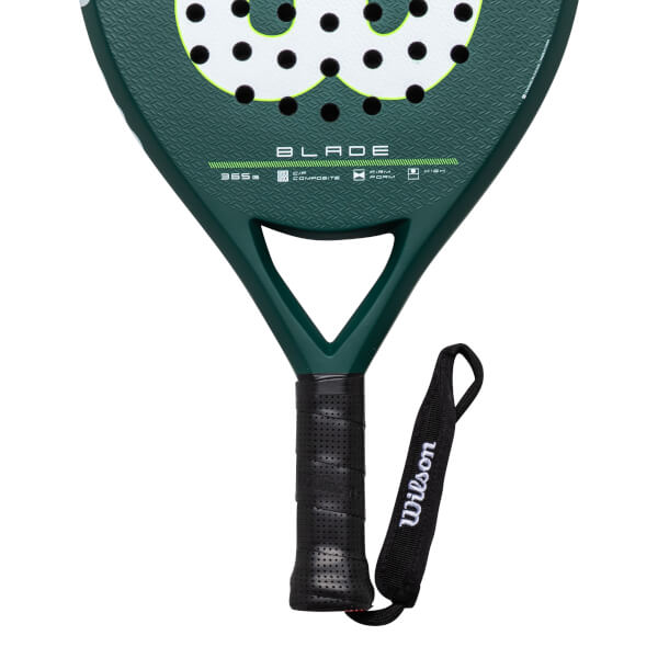 Close-up of the handle and lower head of a green Wilson Blade paddle, showing the black grip and wrist strap with "Wilson" text.