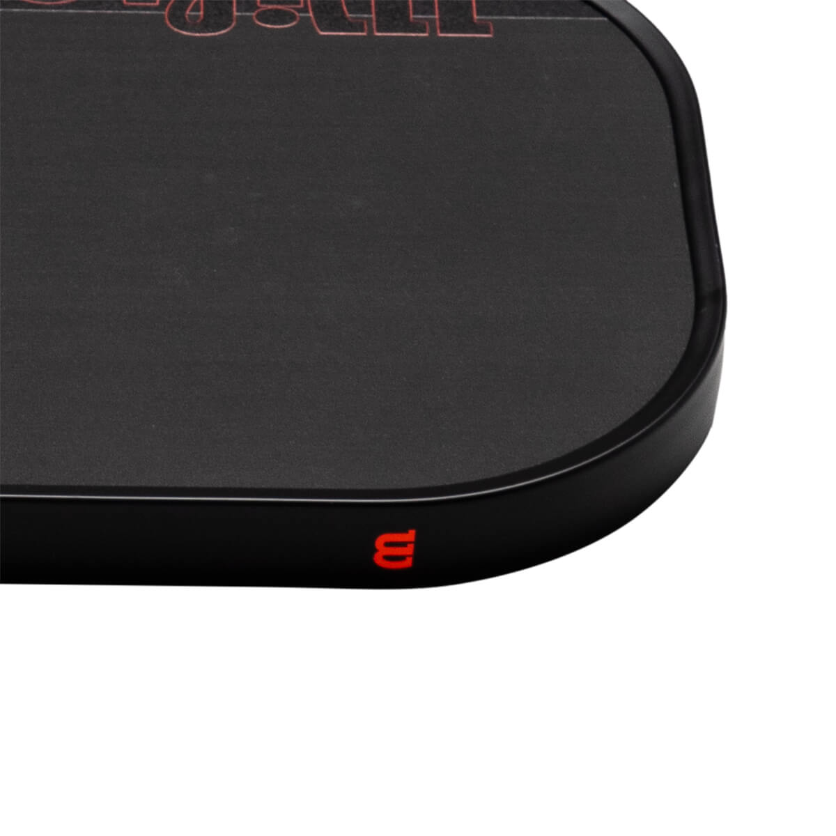 Close-up corner view of a matte black pickleball paddle featuring a red Wilson logo on the edge guard and red "STAFF" text on the face.