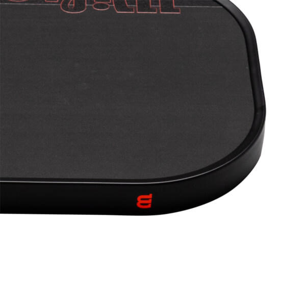 Close-up corner view of a matte black pickleball paddle featuring a red Wilson logo on the edge guard and red "STAFF" text on the face.