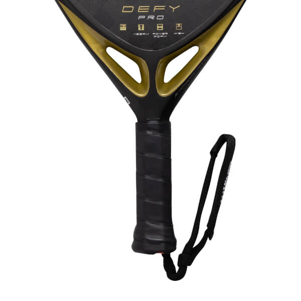 Close-up of a black and gold padel racket with a textured black grip, black wrist strap, and gold DEFY PRO branding.